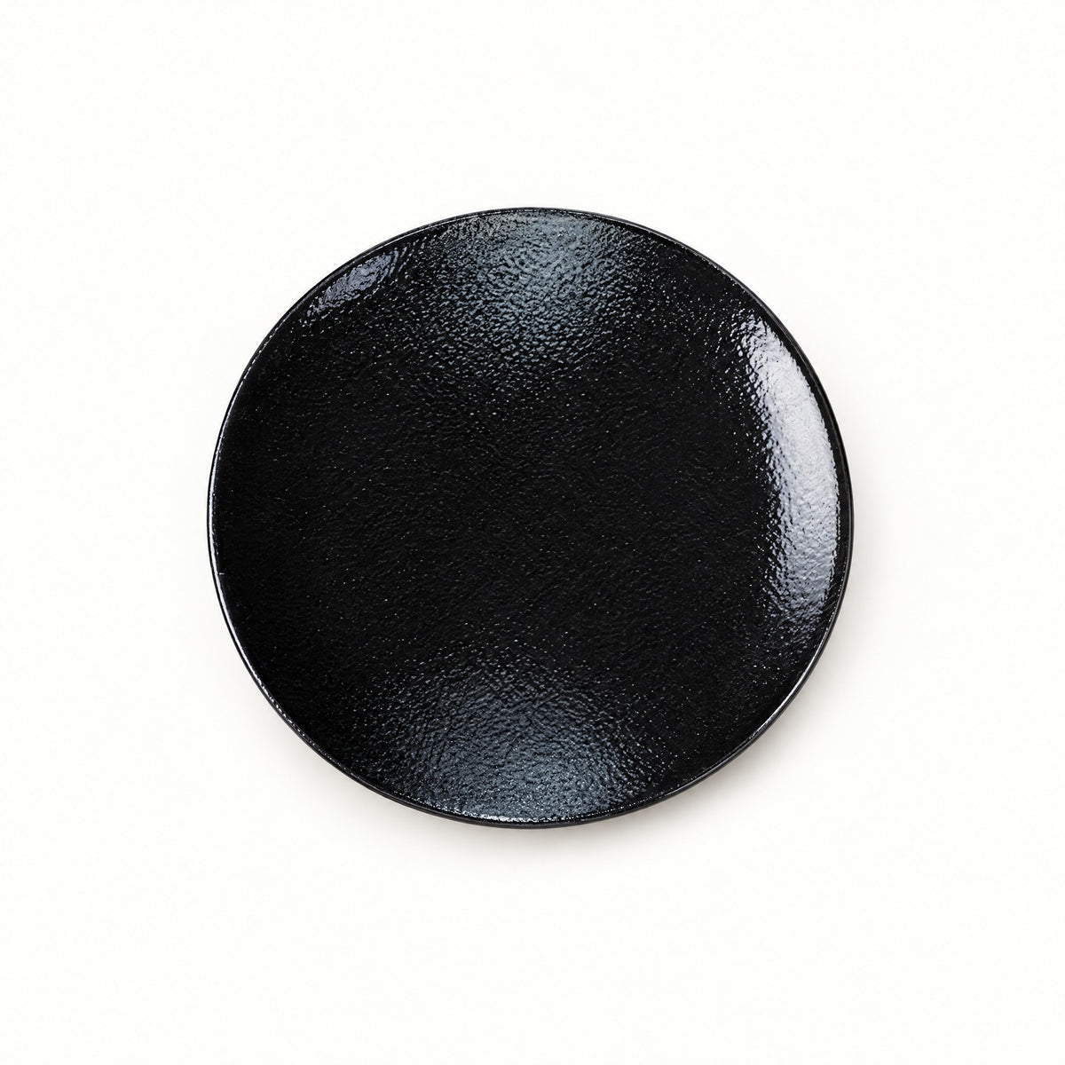 Japanese ceramic shallow plate in a glossy black glaze, seen from above on a plain background