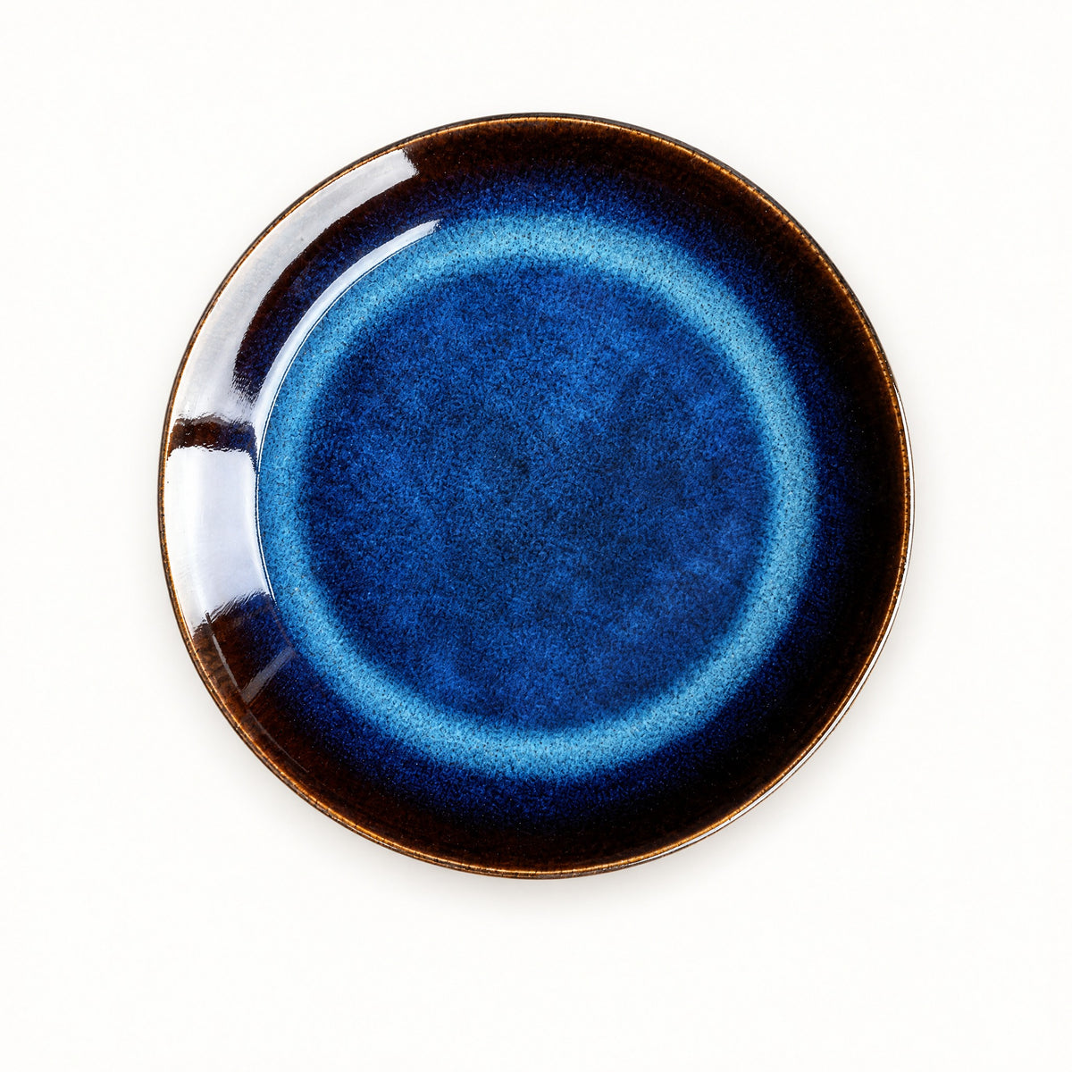 Blue kiln ceramic shallow dish seen from above, deep cobalt glaze pooling in the centre inside an amber-brown rim