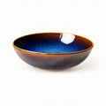 Blue kiln ceramic shallow dish seen from a low angle, showing its depth and the amber-brown exterior