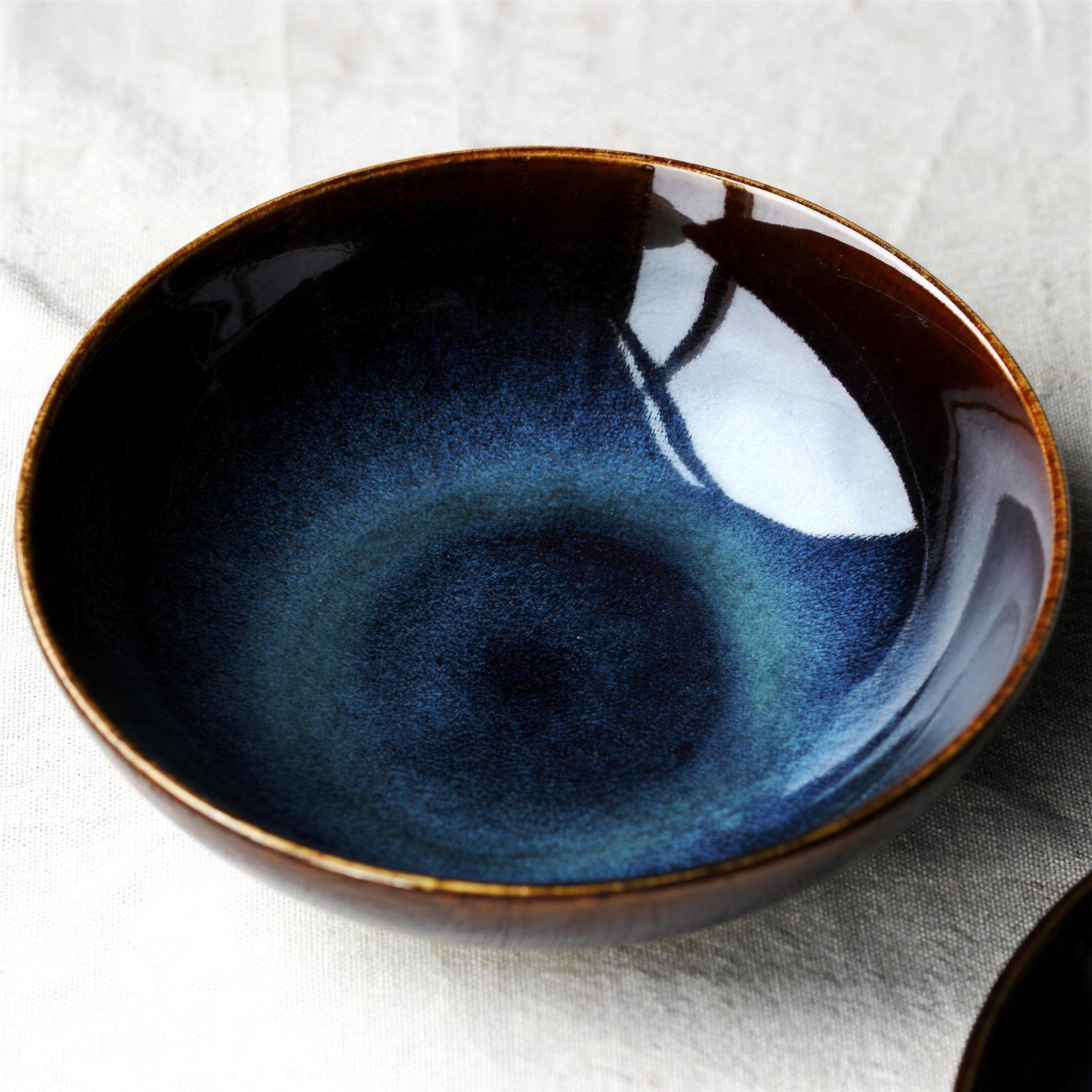 Kiln-glazed blue porcelain shallow dish on a neutral table — detail view