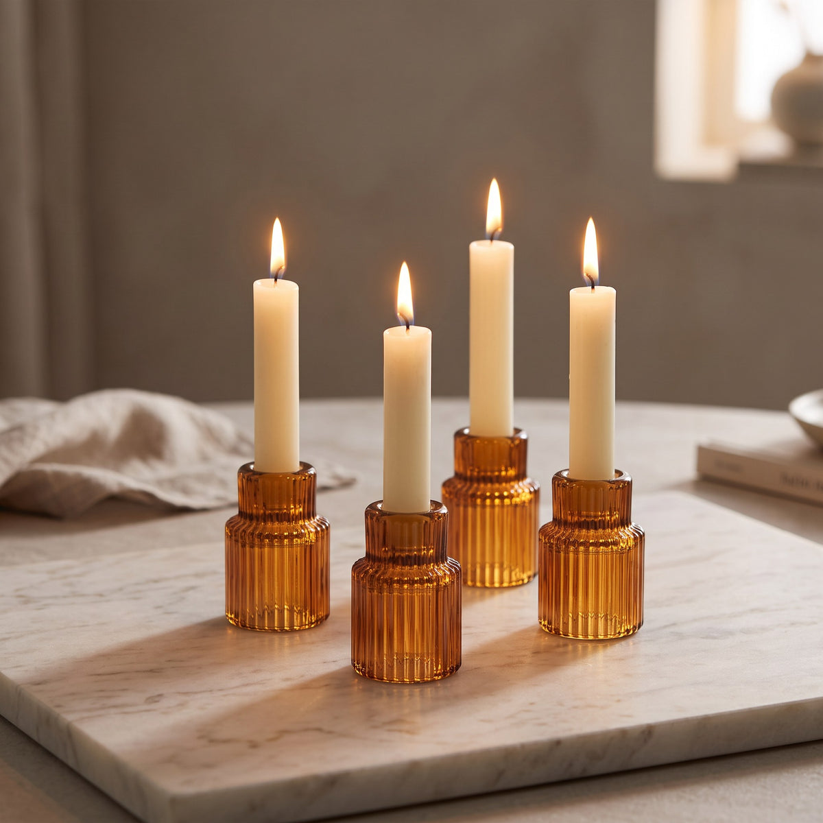 Amber ribbed glass taper candle holders with lit ivory candles on cream marble