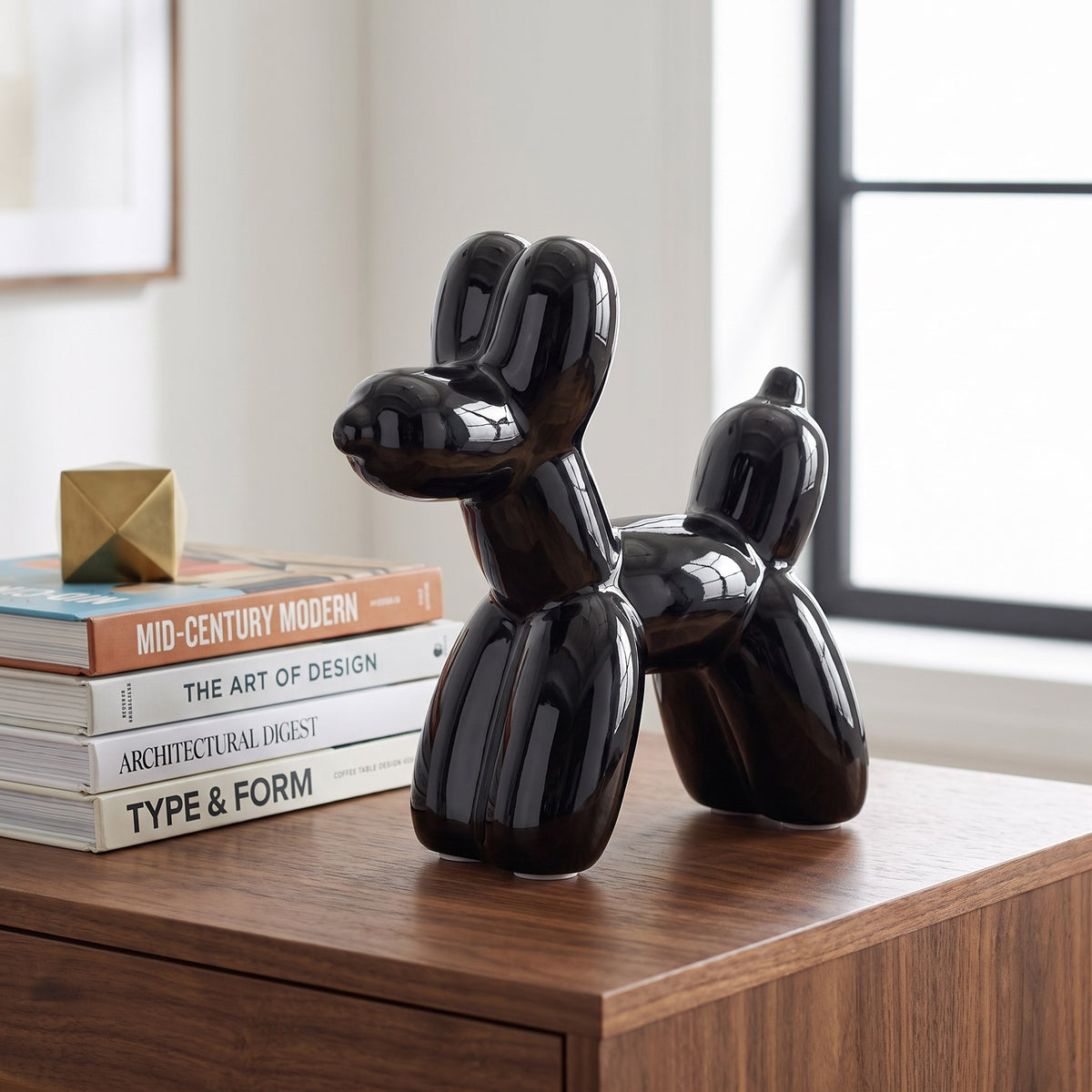 Glossy black ceramic balloon dog sculpture on a walnut desk beside design books