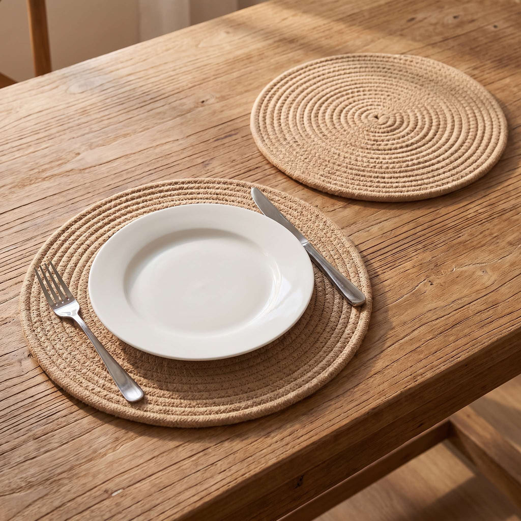 Woven cotton rope placemats on a wooden dining table with a white ceramic plate