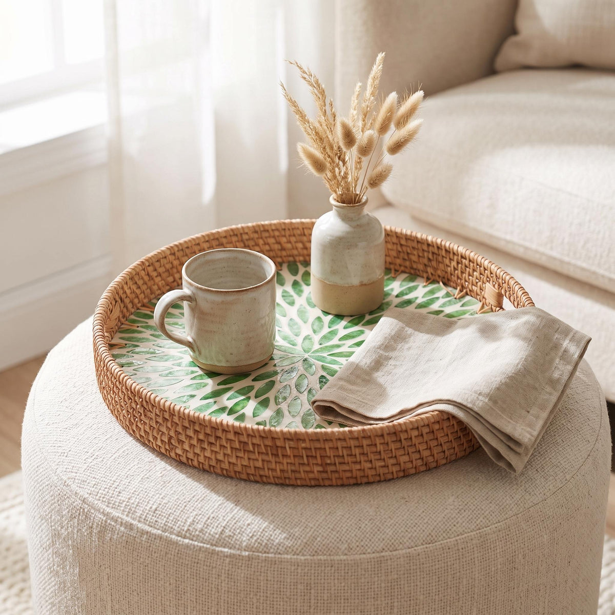 Woven rattan tray with pearl inlay on a cream ottoman holding a mug and vase