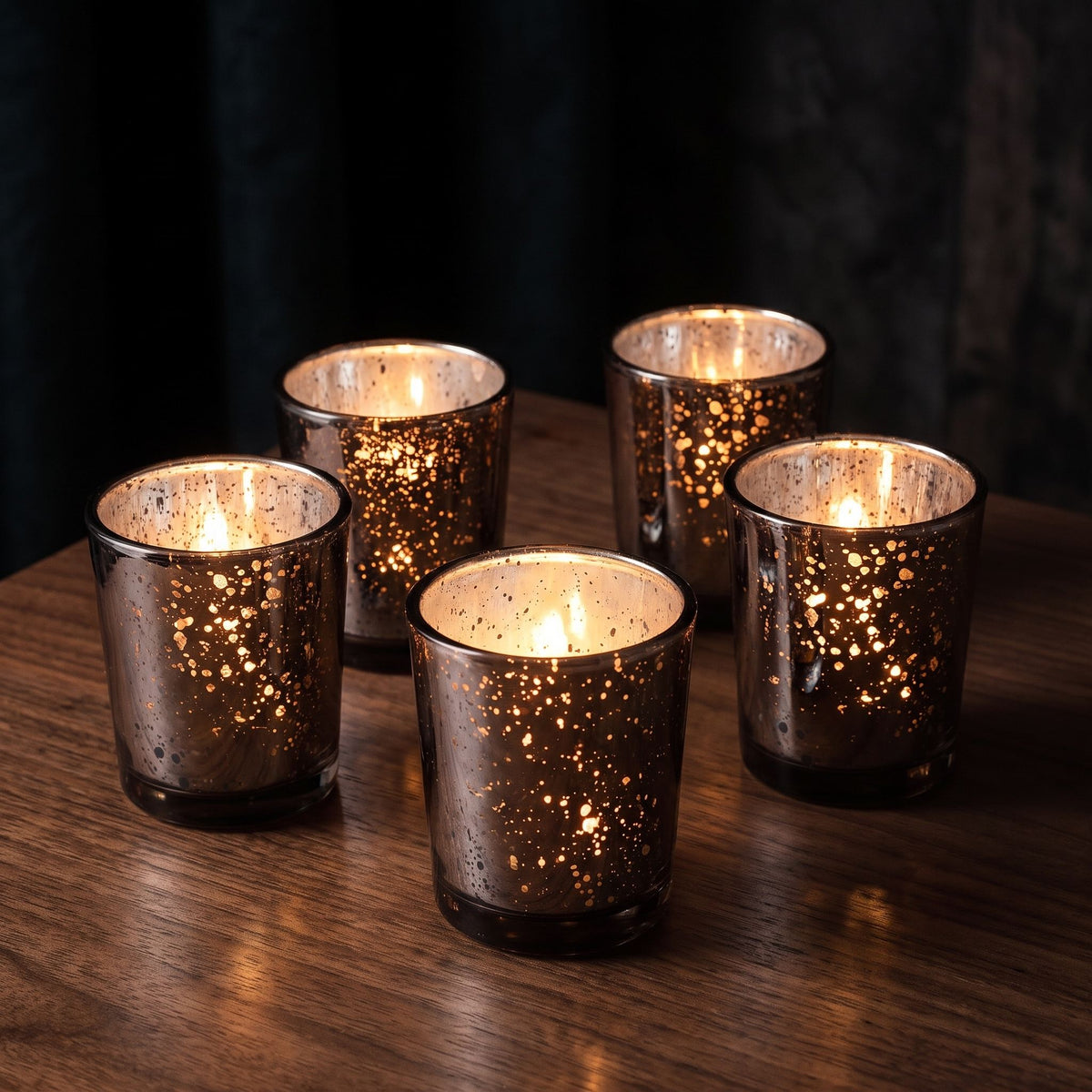 Black speckled mercury glass votive holders with lit tealights on a walnut table